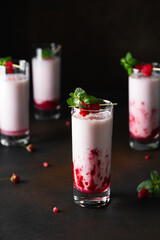 Raspberry milkshake or smoothie in a glasses decorated with mint and raspberries on a black background.