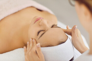Relaxed woman relieves stress while receiving professional facial and head massage in spa salon....