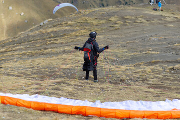 Young man in black with backpack and his paraglider extended ready to jump in the Italian alps.