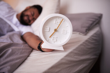 5am clock face in focus with an exhausted man sleeping in bed
