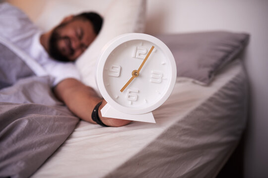 5am clock face in focus with an exhausted man sleeping in bed