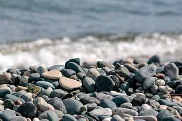 Close-up of stones and pebbles in front of blurry sea water at the beach in sunlight