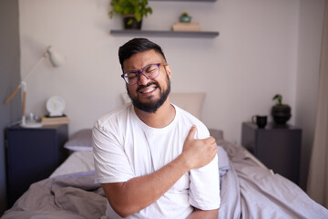 A man clutches his shoulder in pain after waking up in his bedroom