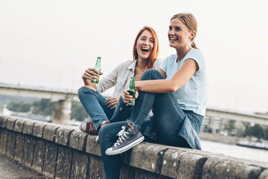 Two female friends are sitting on dock ,relaxing and drinking beer.	
