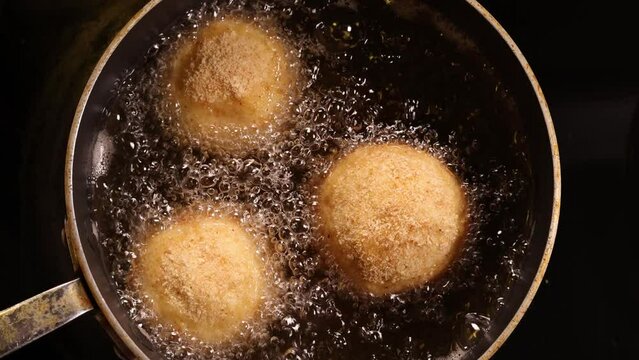Three Italian arancini rice balls deep frying in hot boiling oil, top view of the pan.