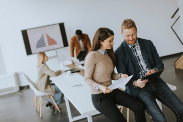 Young entrepreneur couple sitting together on a desk and using digital tablet in the modern office