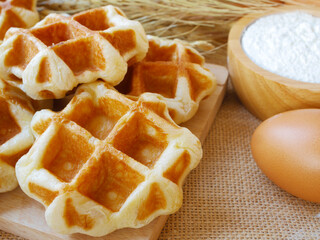 Yummy homemade circle waffles on wooden cutting board with cup of flour and egg