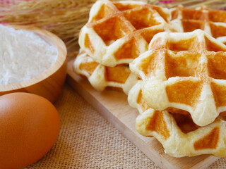 Delicious some waffles on wooden cutting board with cup of flour and egg