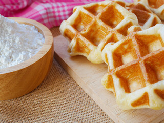 Delicious homemade waffles on wooden cutting board with cup of flour