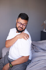Obraz premium A man sits on the edge of his bed holding his shoulder in pain