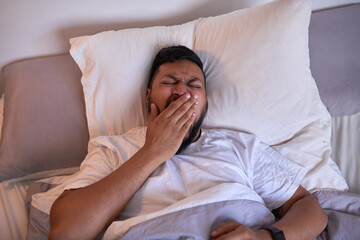 A multi-ethnic adult man yawns in bed as he wakes up