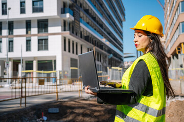 Busy Hispanic female inspector using laptop at construction site