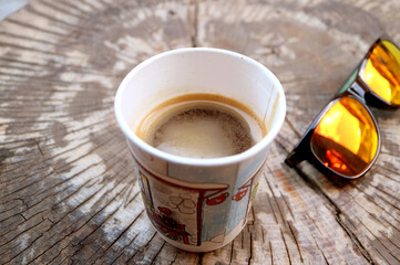 Hot Coffee in a Paper Cup on Tree Stump Table with Sunglasses