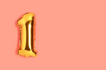 Number 1 golden balloon with copyspace. One year anniversary celebration concept on a coral colored background.