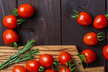 Red tomato and rosemary on cutting board on wooden table. Organic healthy food. Cooking Ingredients