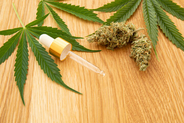 Fototapeta premium Medical cannabis concept image. Hemp leaves, buds and pipette on wooden background