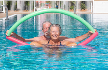 Cheerful adult happy senior couple having fun in outdoors swimming pool doing exercise with swim...