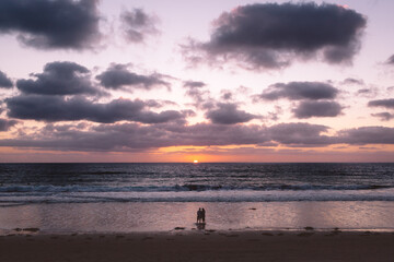Fototapeta na wymiar Couple stands on beach at sunset as sun dips below horizon