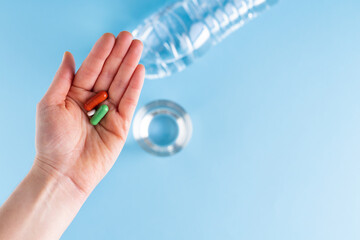 Hand showing three pills with bottle and glass of water on blue background. Health and medicine concept.