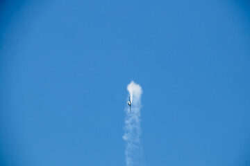 Stunt plane spouting smoke looping and flying sideways in blue sky - Copy space