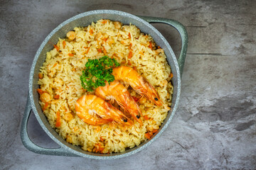 Rice with shrimps in a frying pan on a wooden table, top view.