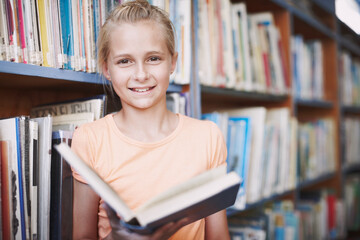 Ill be a writer one day. Portrait of a cute young girl reading a book in the library.