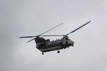 close up of an RAF Chinook tandem-rotor CH-47 helicopter flying fast and low in a cloudy blue grey sky on a military battle exercise, Wilts UK - obrazy, fototapety, plakaty