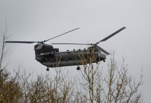 close up of an RAF Chinook CH-47 helicopter banking hard and flying low in a cloudy blue grey and white winter sky on a military exercise, Wiltshire UK