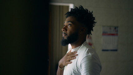 A pensive young black man standing by window thinking about life