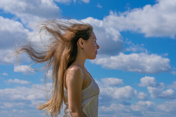 Young long blond haired woman watching happily far to horizon, concept of future, opportunities, inspiration and calmness.Bright blue summer sky with fluffy white clouds