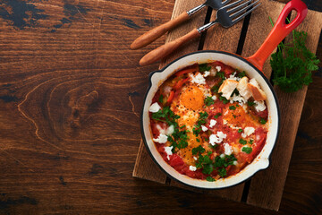 Shakshuka. Homemade fried eggs poached in sauce of tomatoes, olive oil, peppers, onion and garlic in iron frying pan on old wooden background. Traditional cuisine of Israel. Late breakfast concept.
