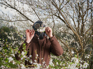 Man allergic suffering from seasonal allergy at spring, posing in blossoming garden at springtime....