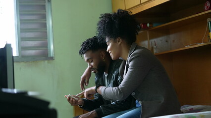 A black couple looking at smartphone device together in bedroom