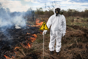 Firefighter ecologist extinguishing fire in field. Man in protective radiation suit and gas mask...