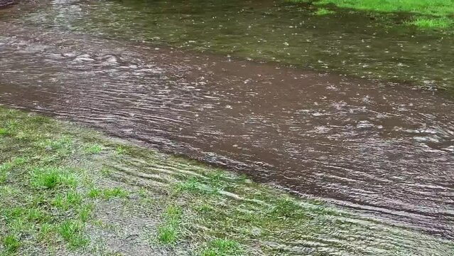 Slow motion of excess rainwater flooding over a gravel path and grass lawn on both sides, public park and recreation area

