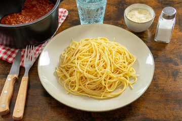 plate of plain spaghetti with a pot of bolognese on a table