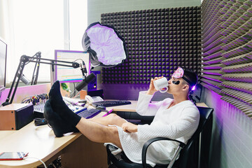 A funny radio presenter in a sleep mask, bathrobe and cosmetic patches - obrazy, fototapety, plakaty