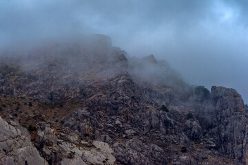Stony slopes of mountain in dense fog.