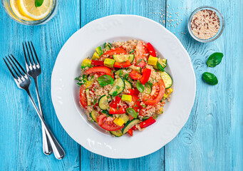Tabbouleh salad with quinoa, tomatoes, cucumber, avocado, red pepper and fresh herbs on a blue background.