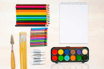 Watercolor oil paints, paintbrushes, colorful pencils, pastel crayons,blank watercolor paper pad. Creativity creation process. Artist's stuff on white table.Top view Flatlay of drawing supplies