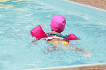 Criança com boia rosa na piscina nadando.