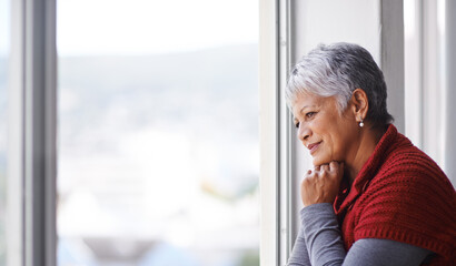 Lost in thought. Shot of a mature woman standing by a window on a sunny day.