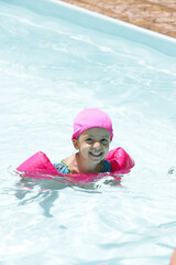 Fototapeta na wymiar Criança na piscina a nadar com flutuador rosa com água azul. 