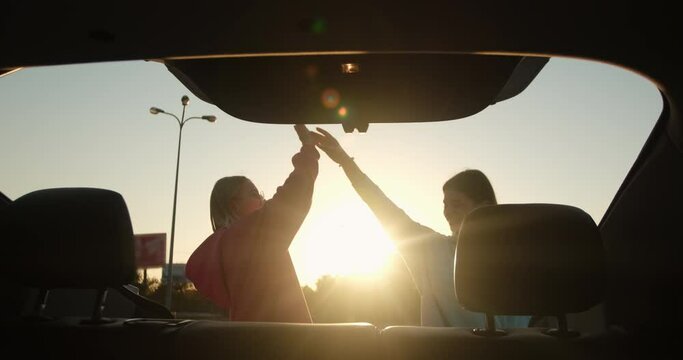 Women open car trunk and put bags inside giving high five. Girl friends smile feeling happiness and excitement after shopping and bargains at sunset