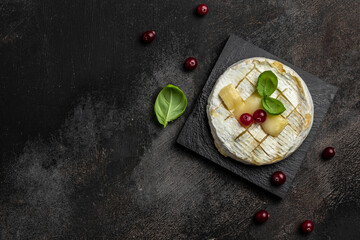 French cuisine. Baked camembert cheese with cranberries and basil leaves on a dark background, Long banner format. top view