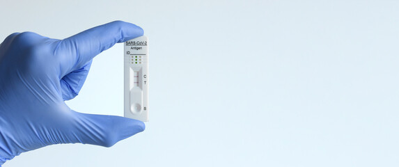 una mano con un guante azul de látex cogiendo un test de antígenos positivo sobre fondo azul claro. test covid-19 y corona virus. con copyspace. 