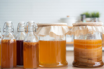 Homemade fermented raw kombucha tea, variety of flavors in bottles and glass jars mix with a fruit juice and scoby on wooden table. Healthy natural probiotic drink.