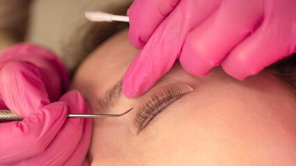 Woman on the procedure for eyelash extensions, lamination in beauty salon. Cosmetologist applying glue on woman's lashes. Close-up of girl face during lash lift laminating botox set.  - obrazy, fototapety, plakaty