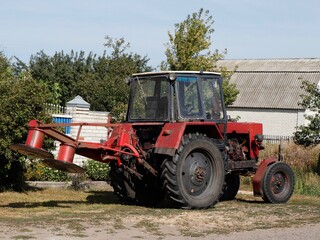 Obraz premium Red tractor with mowing machine in the village.