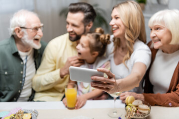 blurred woman taking selfie with cheerful family during easter dinner.